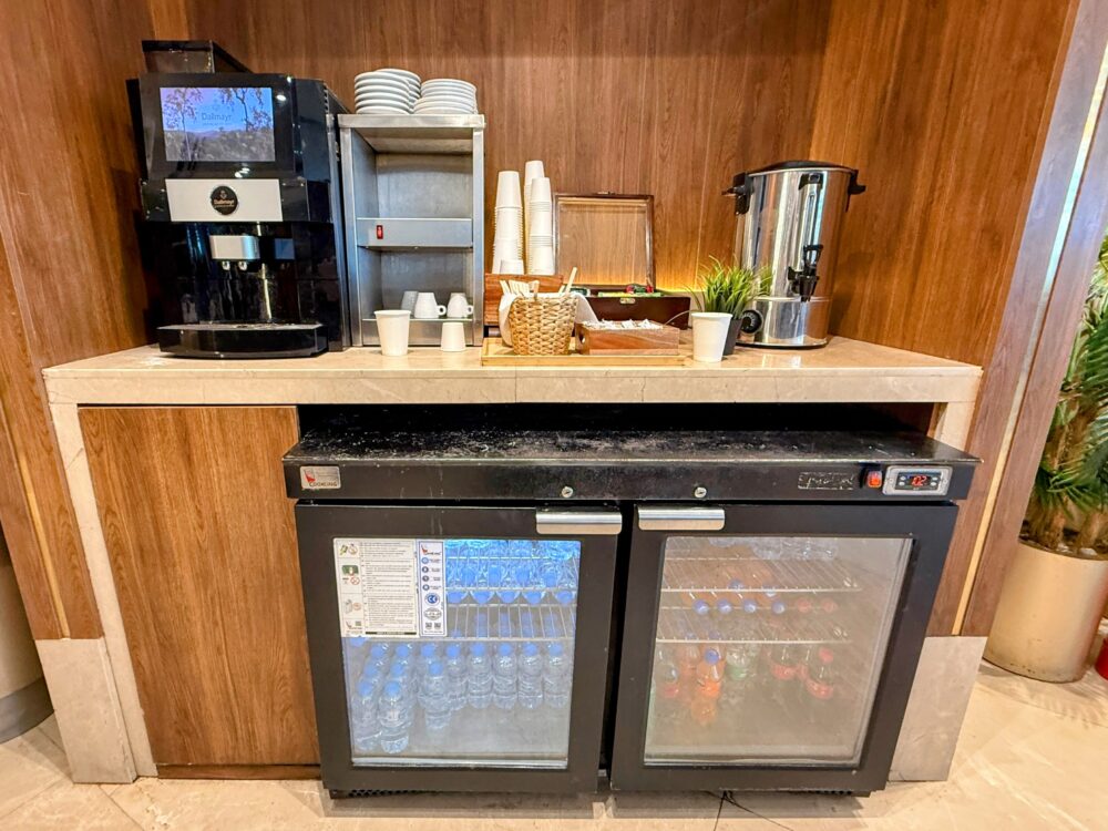 全自動コーヒーマシンと紅茶用の熱湯サーバー、下のガラス扉付き冷蔵庫に冷えたドリンクが並ぶドリンクステーション。