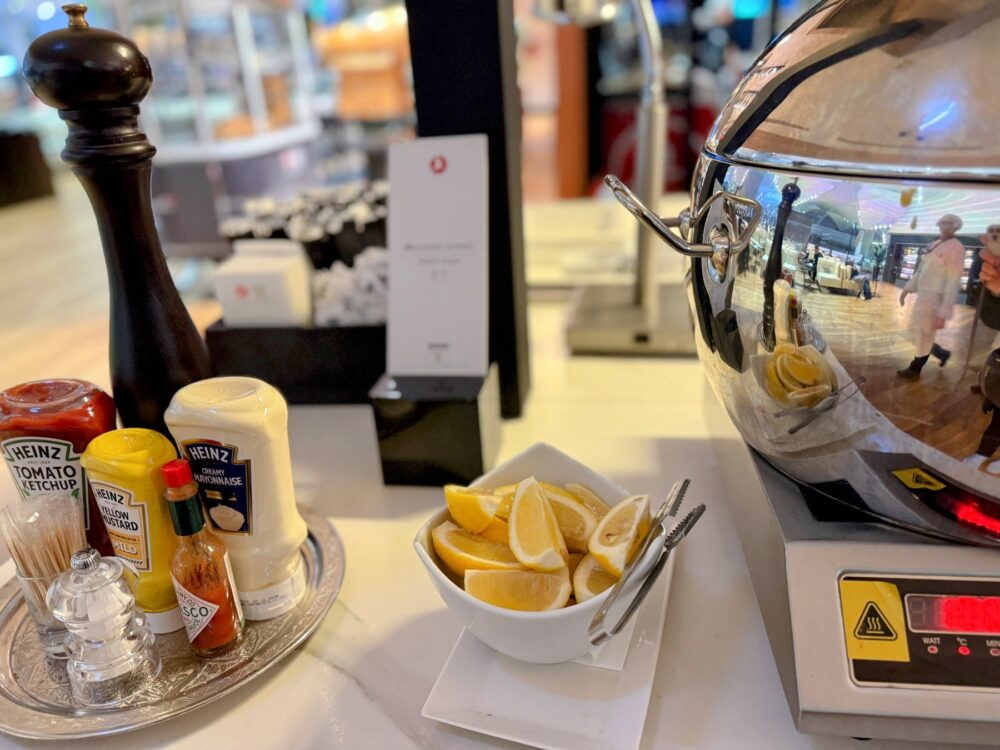 スープや料理の保温容器の横に置かれた、レモンのスライス、ケチャップ、マスタードなどの調味料セット