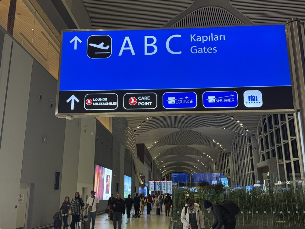 空港ターミナル内の案内板。ABCゲートへの方向とラウンジ、シャワー施設への道順が示されている