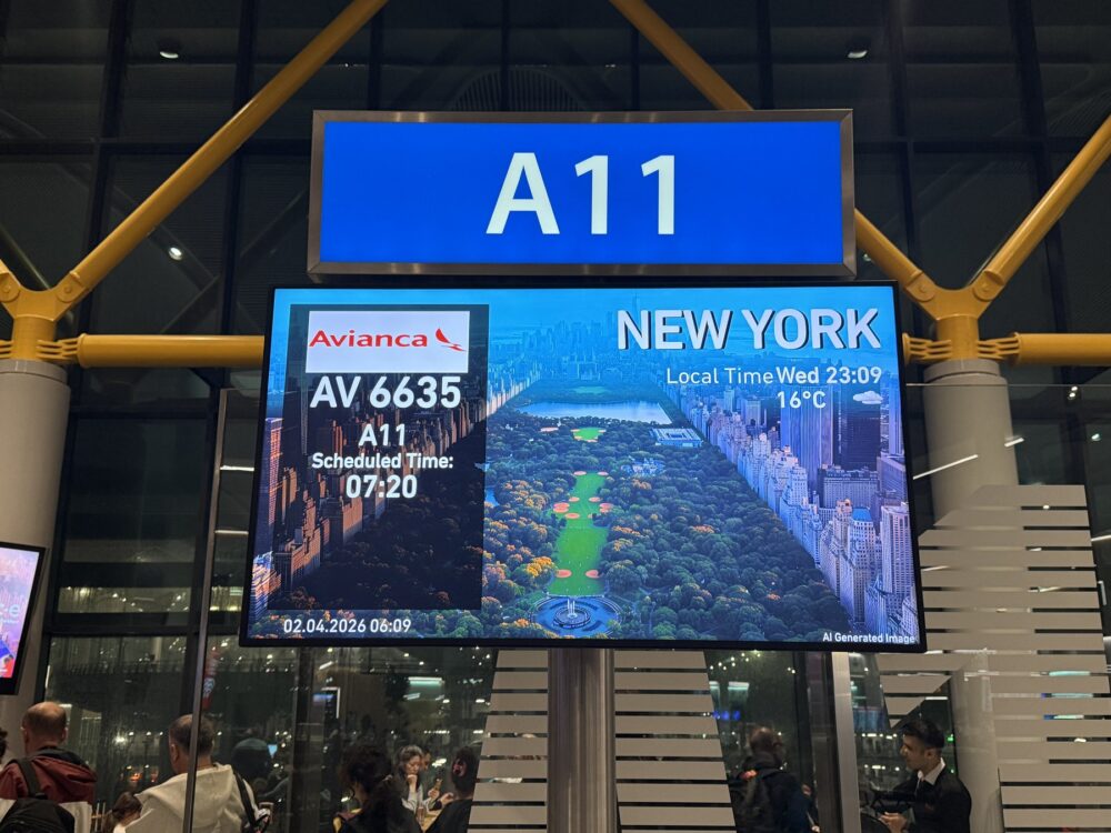 A11ゲートのフライト案内掲示板。Avianca航空AV6635便ニューヨーク行きの出発情報と、セントラルパークの風景写真が表示されている