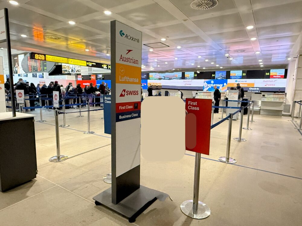 エア・ドロミティ、オーストリア航空、ルフトハンザ、スイス航空のロゴが並ぶ案内サインと、「First Class」の赤いプレートが立つスターアライアンス上級会員専用チェックインカウンター。