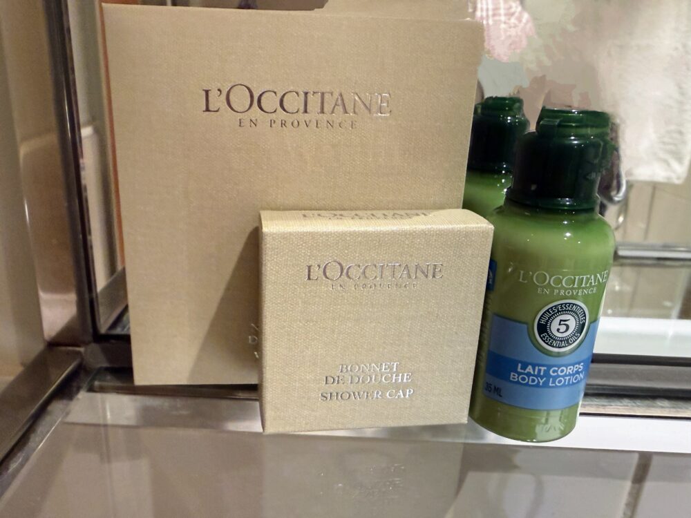 バスルームに用意されたロクシタン(L'OCCITANE)のシャワーキャップ、ボディローション、アメニティボックス