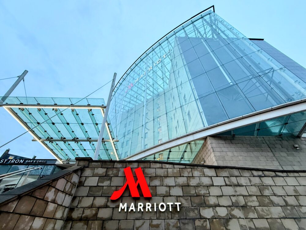 ホテルの象徴的なガラス張りの外観と、手前の石垣に掲げられた「MARRIOTT」の赤いロゴサイン
