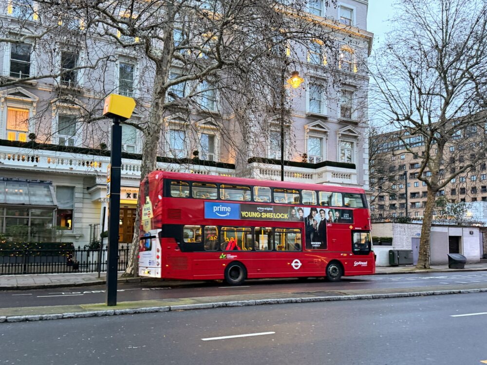 ロンドンの街中を走る特徴的な赤い二階建てバス(ダブルデッカー)の側面と周囲の街並み