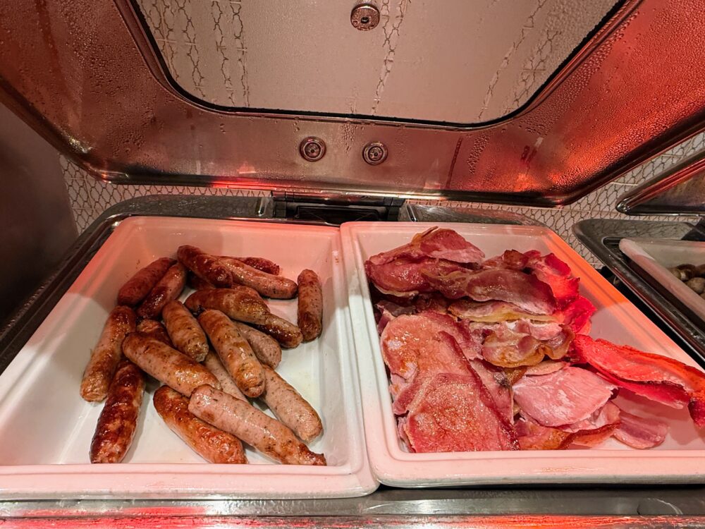 温かいビュッフェカウンターに用意された、焼き色のついたソーセージとカリカリのベーコン