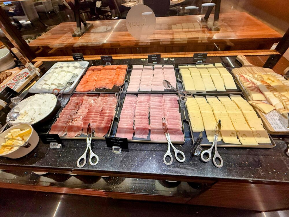 生ハム、スモークサーモン、ハム、数種類のチーズがトレイに整然と並ぶ朝食ビュッフェのコールドカットコーナー