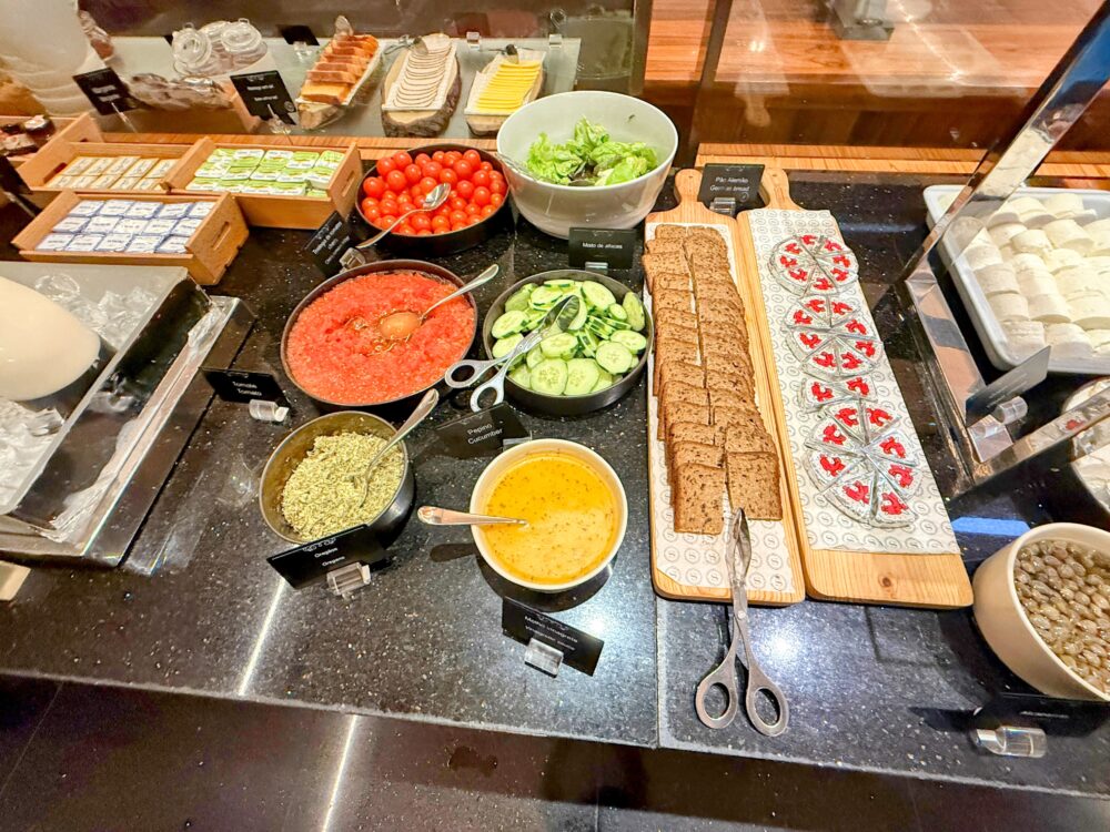 ミニトマト、きゅうり、すりおろしトマト、ライ麦パン、オリーブなどが並ぶ朝食ビュッフェのサラダコーナー