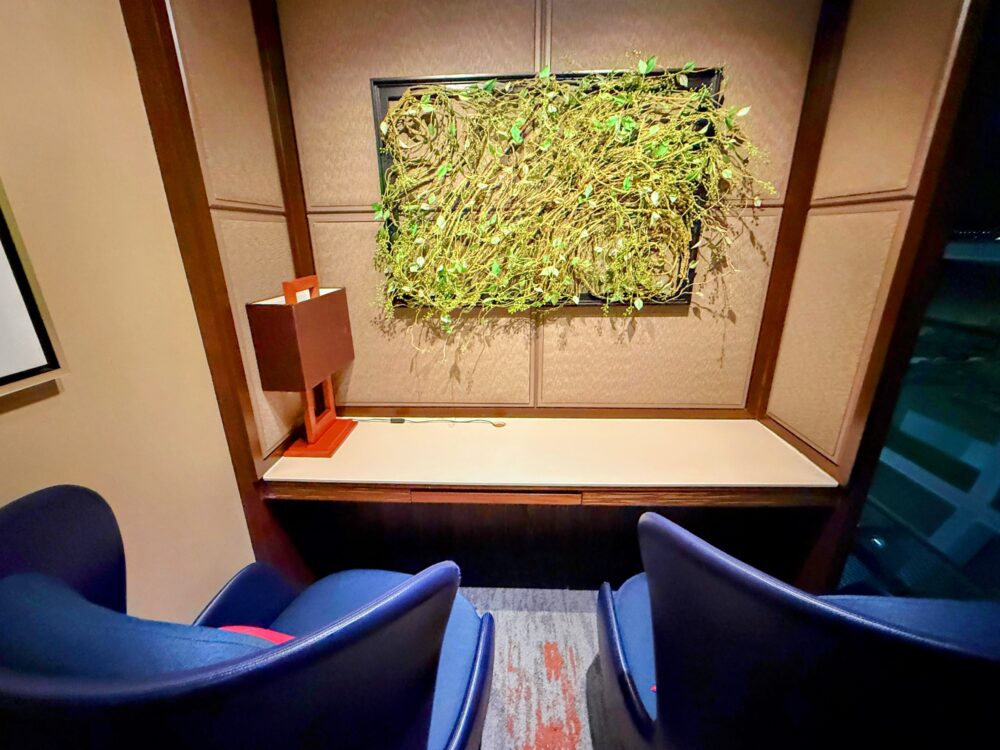 ロイヤルオーキッドラウンジ内の壁面装飾(緑の植物をあしらったアートとデスクランプ)が置かれたワークスペース風の席