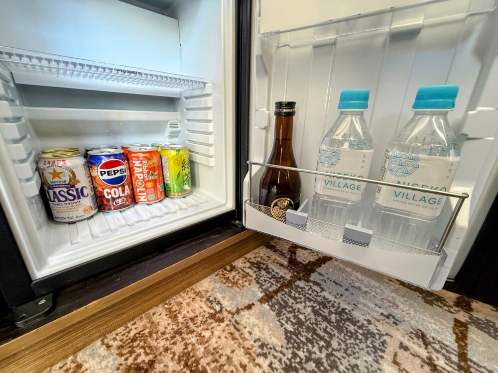 客室冷蔵庫の内部。サッポロクラシックビール、ペプシコーラ、リボンナポリン、緑茶の缶飲料と、ニセコビレッジのミネラルウォーター、瓶ドリンクが綺麗に冷やされている。
