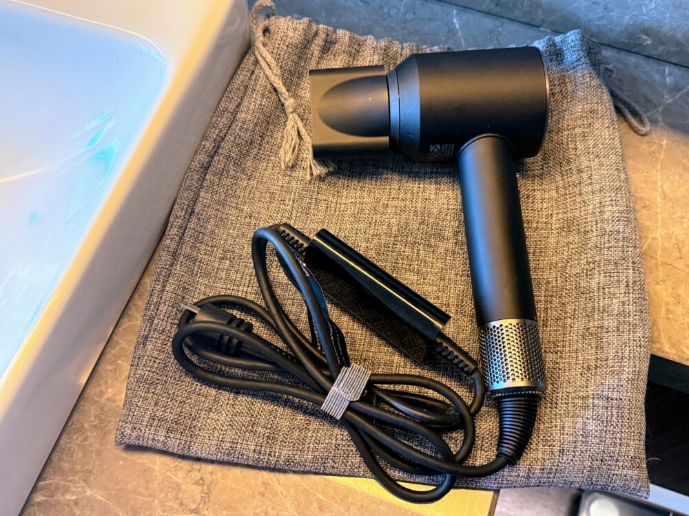 グレーの保存袋の上に置かれた黒い高級ヘアドライヤーと電源コード。スタイリッシュなデザインが特徴。