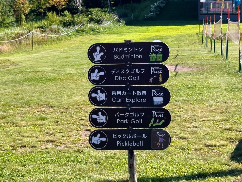 ニセコビレッジのアクティビティ案内看板。バドミントン、ディスクゴルフ、乗用カート散策、パークゴルフ、ピックルボールの5つが矢印で示されている。