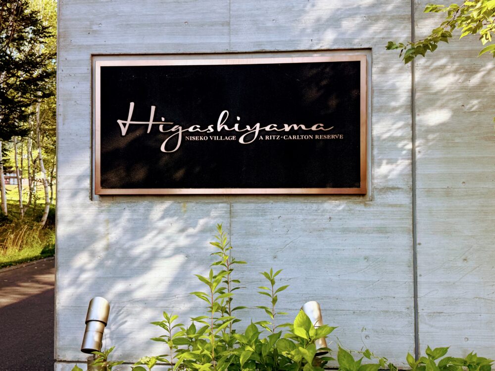 ホテル入口に掲げられた「Higashiyama NISEKO VILLAGE A RITZ-CARLTON RESERVE」のサイン。コンクリートの壁に黒い金属プレートが埋め込まれている。