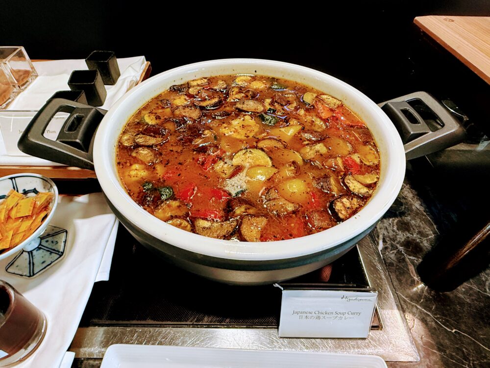 朝食ビュッフェの「Japanese Chicken Soup Curry(日本の鶏スープカレー)」のアップ。野菜やチキンがゴロゴロ入ったスープカレーが、黒いIHヒーターの上に置かれている。