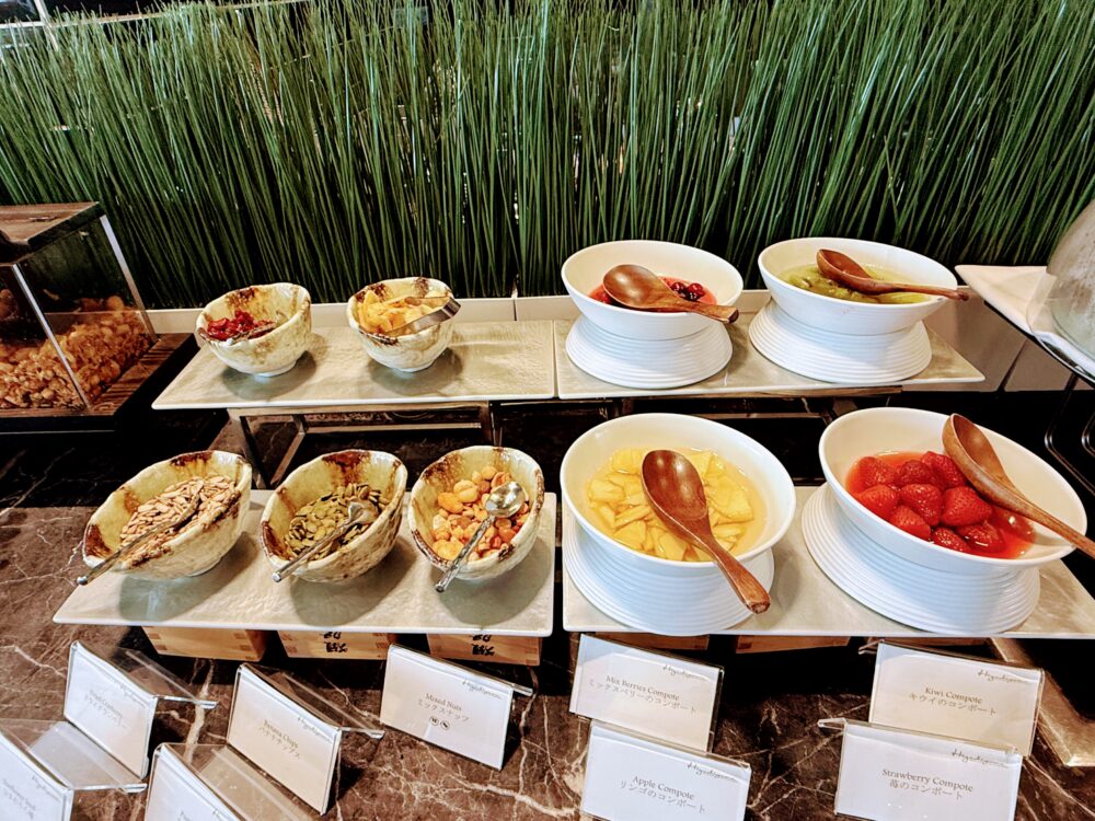 朝食ビュッフェのフルーツコンポートとトッピングコーナー。ボウルに入ったイチゴ、パイナップル、キウイのコンポートや、ナッツ、ドライフルーツが並び、木のスプーンが添えられている。