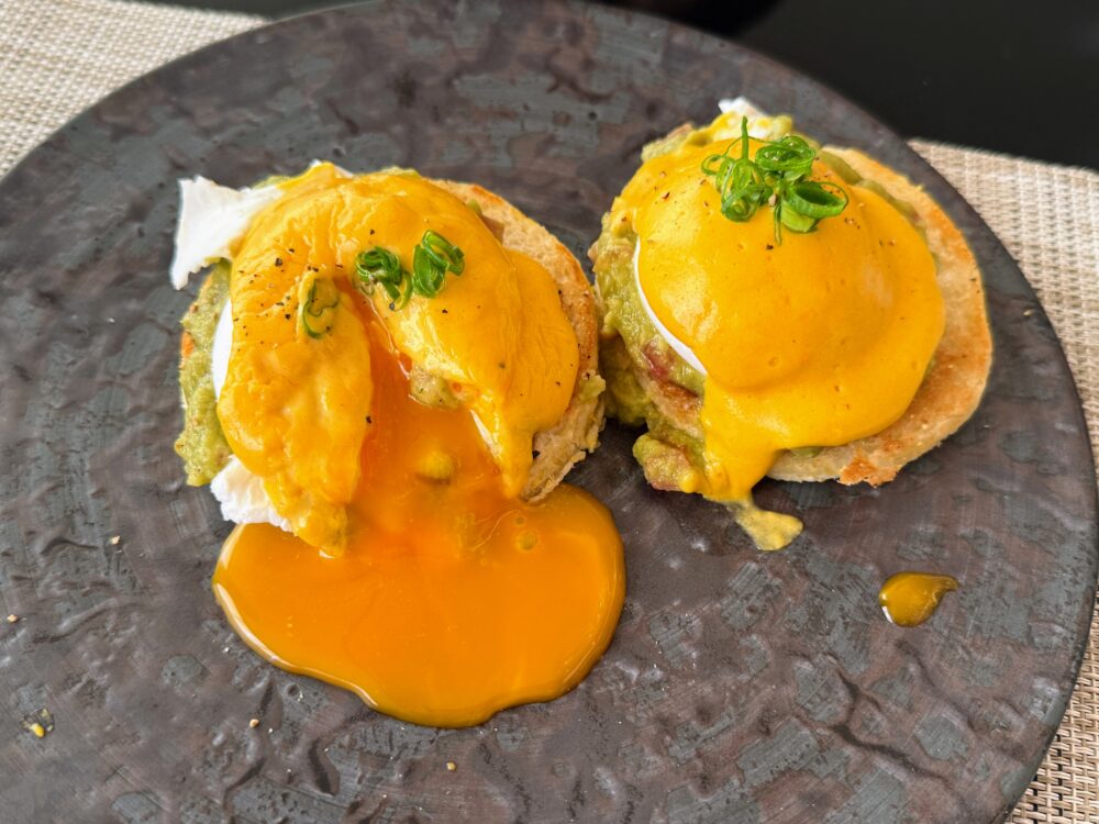 朝食のシグネチャーディッシュ「ニセコ エッグ ベネディクト(ワカモレとトマト)」。イングリッシュマフィンの上にワカモレとポーチドエッグが乗り、トリュフのオランデーズソースがかかっている。切られた卵黄がとろりと流れ出ている。