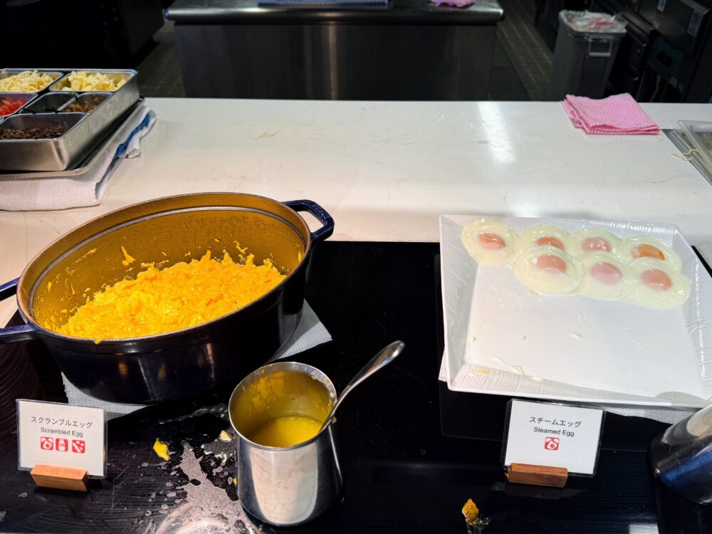 レストランの朝食ビュッフェで提供されている卵料理。STAUB（ストウブ）の鍋に入ったスクランブルエッグと、白いプレートに並べられた目玉焼き（スチームエッグ）。