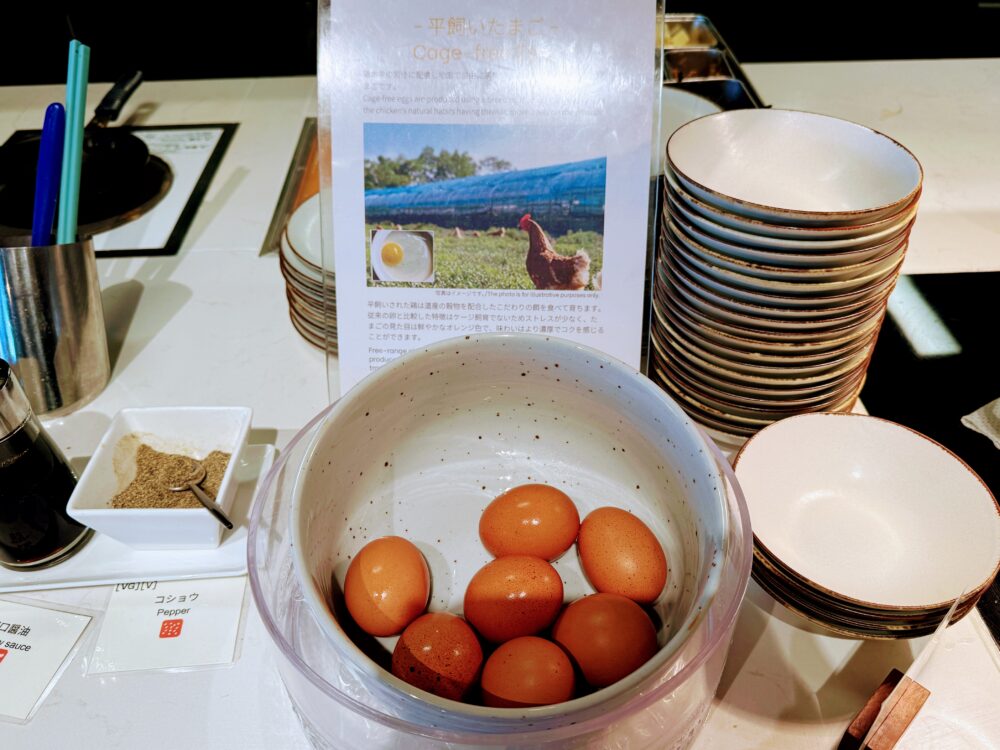 平飼いいたまご（Cage-free Eggs）の案内POPと、新鮮な卵が入れられた大きなボウル、醤油やコショウなどの調味料が置かれたコーナー。