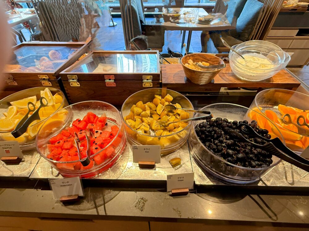 朝食ビュッフェのフレッシュフルーツコーナー。カットされたスイカ、キウイ、オレンジ、グレープフルーツ、ブドウなどが透明なボウルに入れられている。