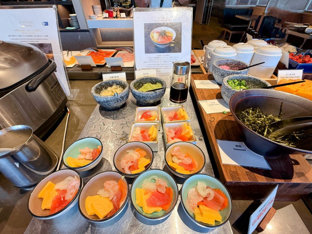 朝食ビュッフェのミニ海鮮丼コーナーの全景。サーモンや甘エビ、ネギトロなどが盛られた小鉢や薬味類が並んでいる。