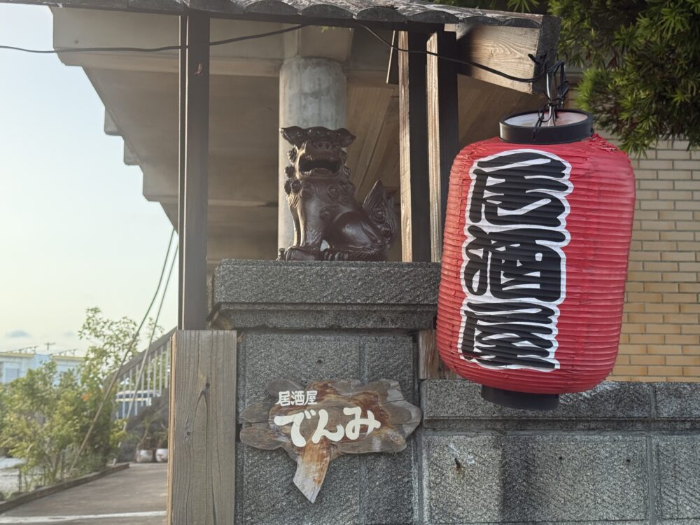 伊良部島の「居酒屋でんみ」の入口。赤い提灯とシーサー、店名の看板がある。