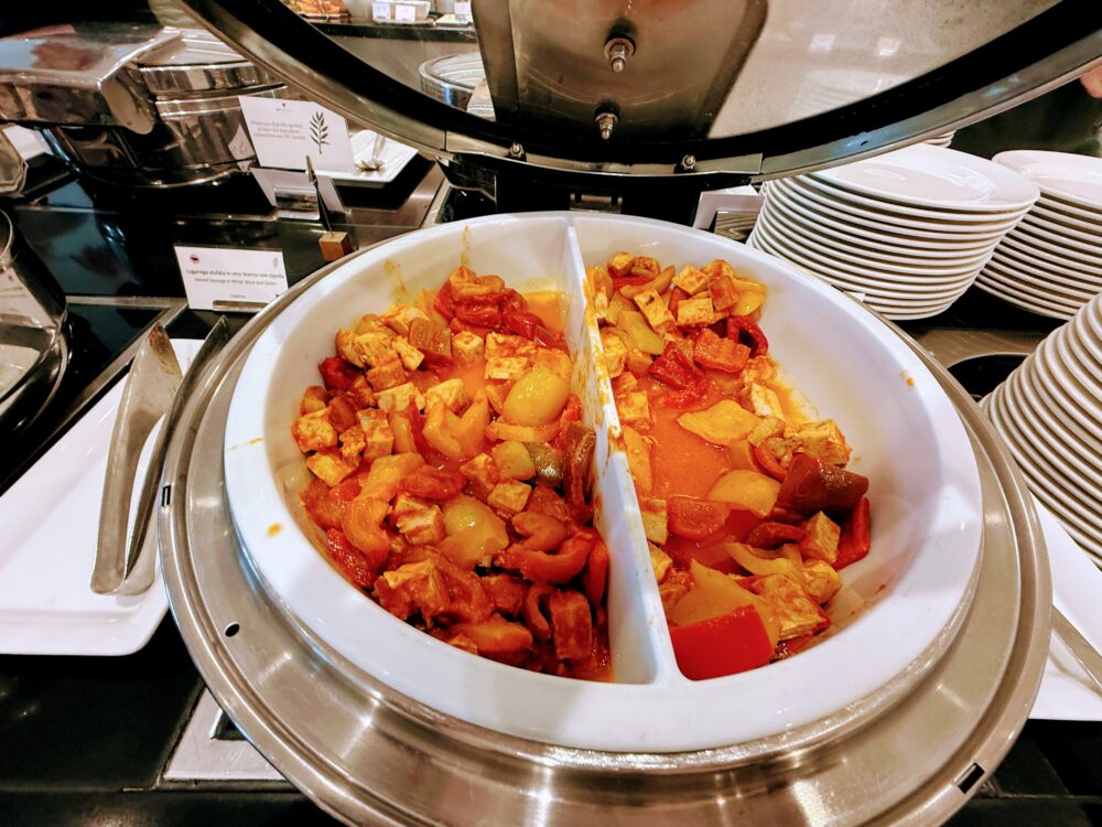 朝食ビュッフェのホットミール。白い保温鍋の中に、トマトソースで煮込まれた豆腐とパプリカの料理（左）と、ソーセージの白ワイン煮込み（右）