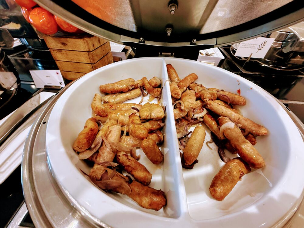 朝食ビュッフェのホットミール。保温鍋にたっぷり入った、こんがりと焼き色のついたソーセージとソテーされたオニオン