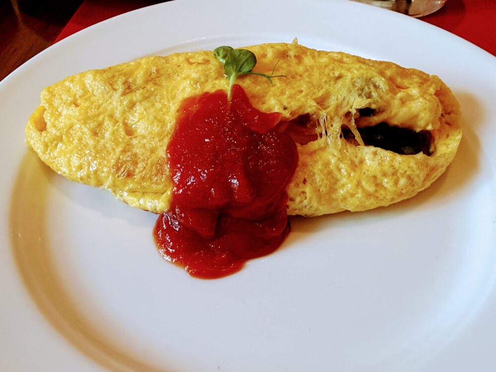 エッグステーションでオーダーした出来立てのオムレツ。たっぷりのトマトソース（ケチャップ）とグリーンのハーブが添えられ、中にはチーズがとろけている