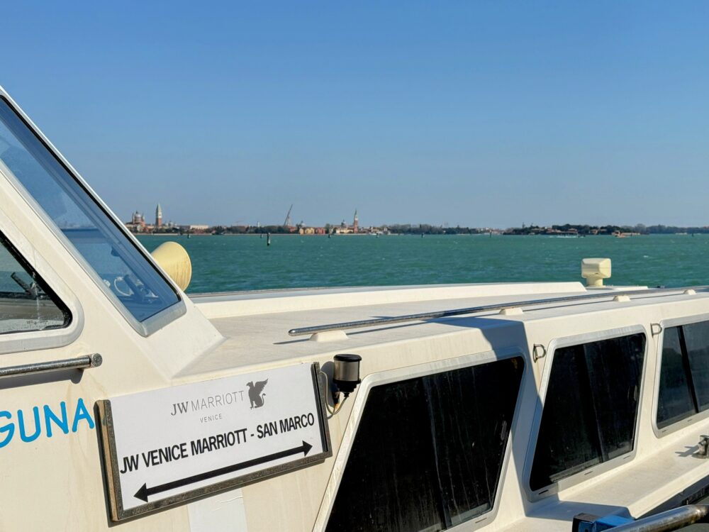 シャトルボートの側面に掲げられた「JW VENICE MARRIOTT - SAN MARCO」の案内板。背景には青いラグーンとベネチア本島の景色