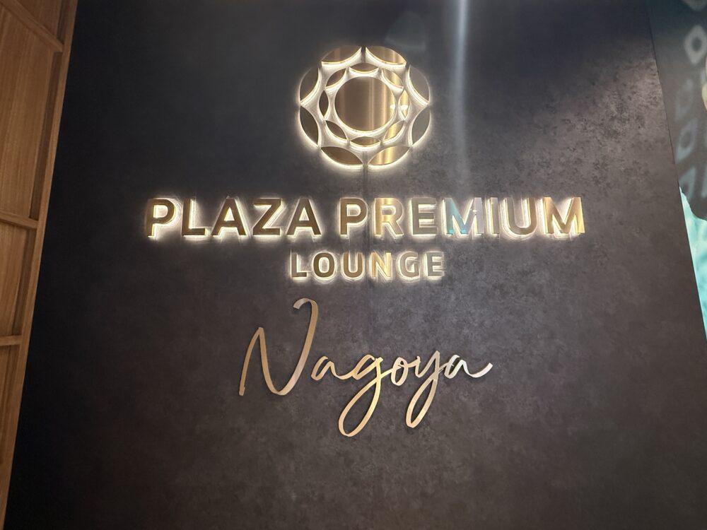 プラザ・プレミアム・ラウンジ名古屋のロゴサイン。黒い壁に金色で「PLAZA PREMIUM LOUNGE」と筆記体の「Nagoya」が輝いている。