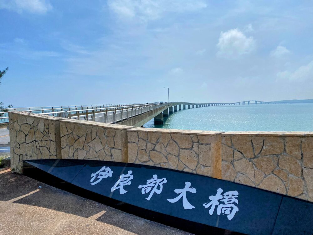 「伊良部大橋」と刻まれた石碑と、宮古島へ続く伊良部大橋。